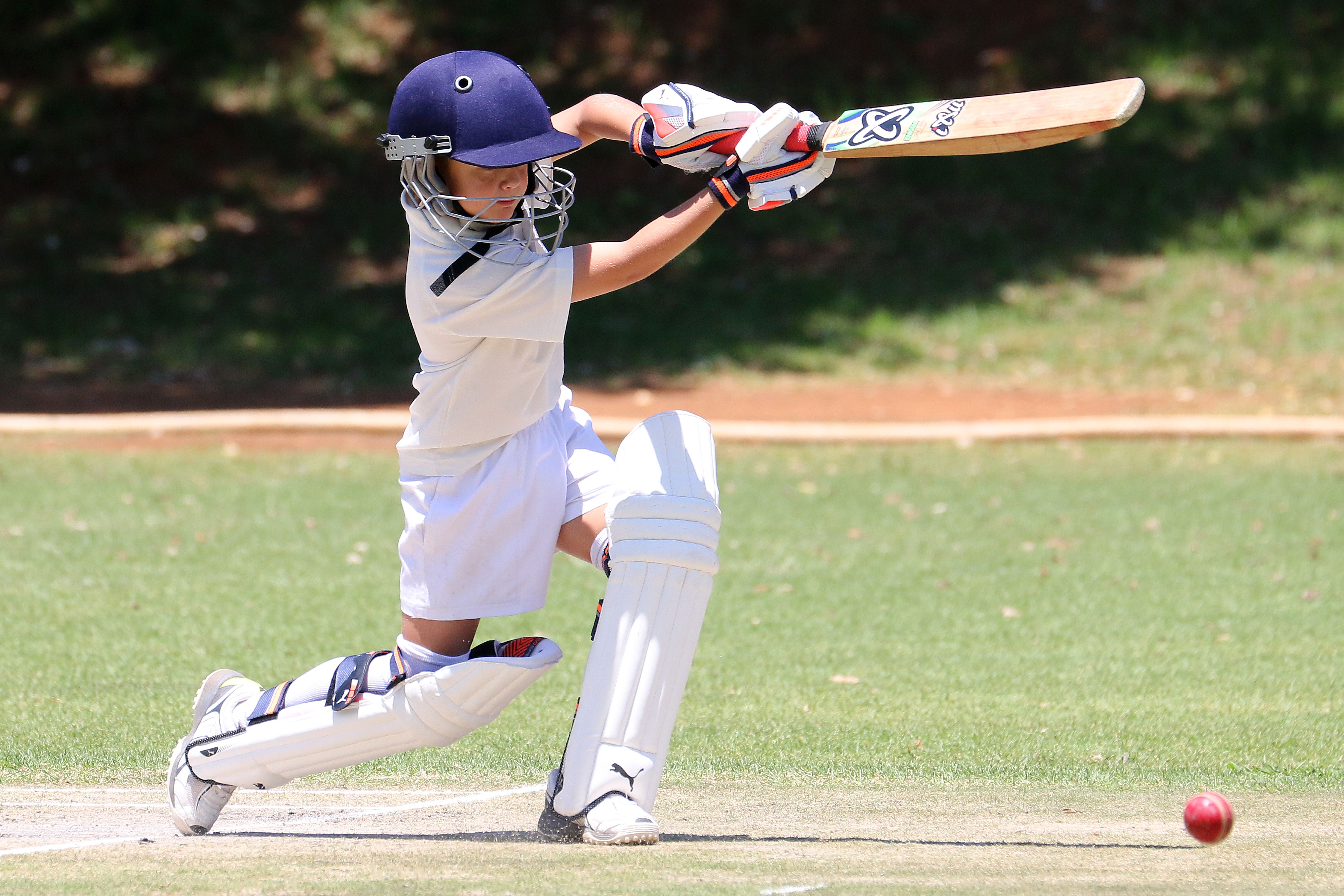 Young cricketer completing a batting shot as the ball rolls away across the outfield