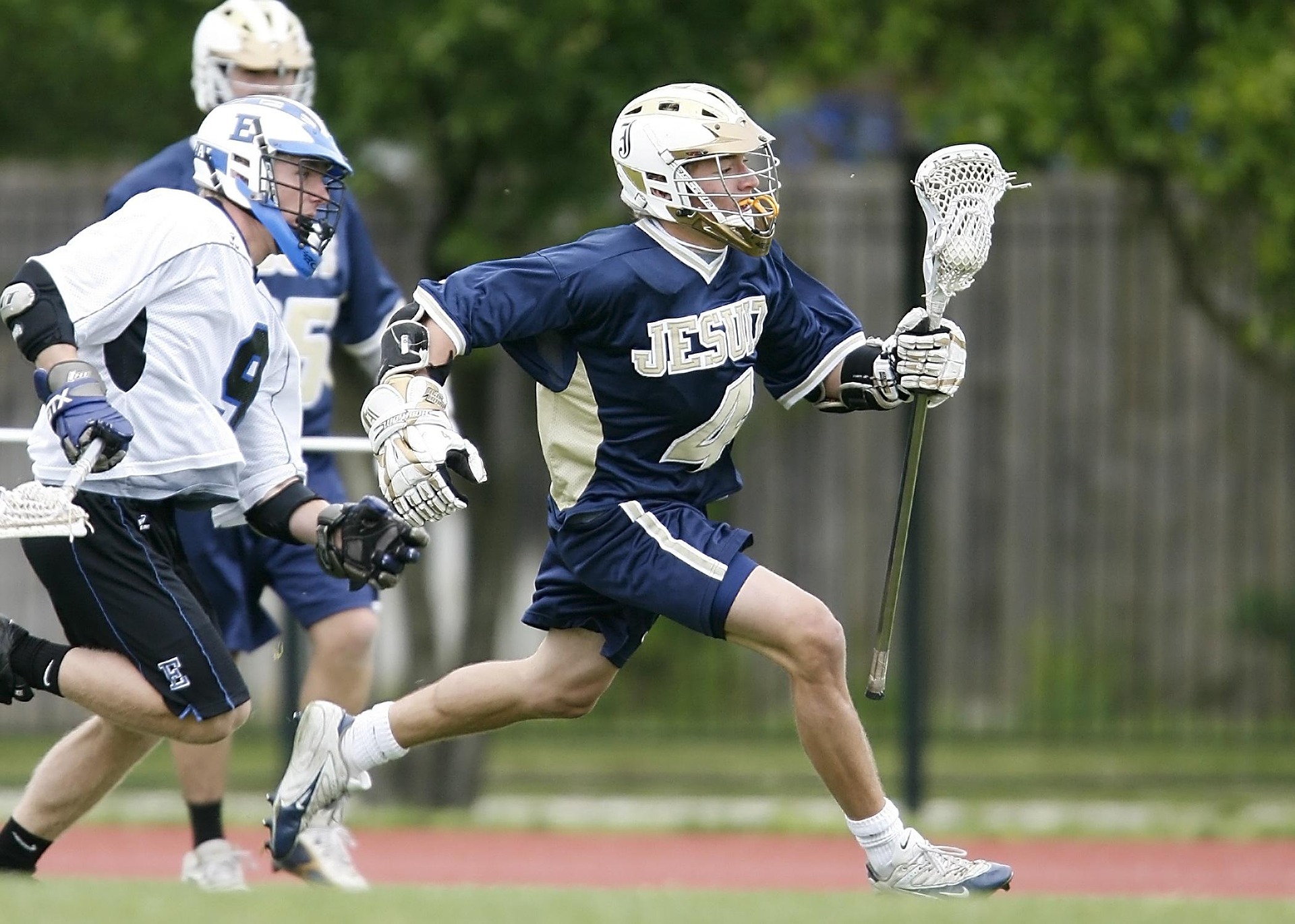A youth lacrosse player sprinting up the field with the ball as defenders give chase